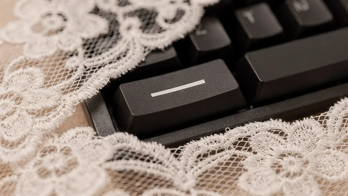 Touche de clavier noire gravée d'un tiret, à demi voilée sous de la dentelle blanche