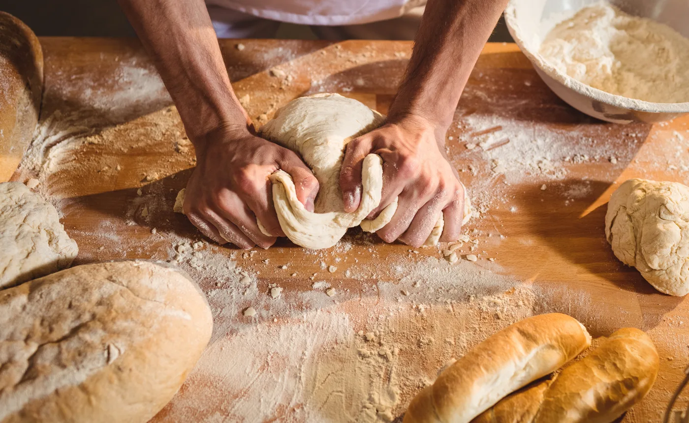Boulanger pétrissant la pâte sur un plan de travail fariné, entouré de pains et baguettes