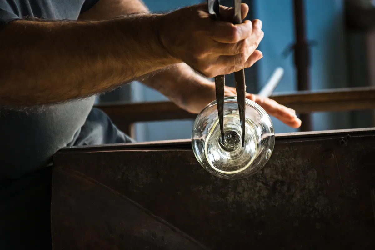 Souffleur de verre façonnant une pièce à l'aide de pinces, geste de précision en atelier