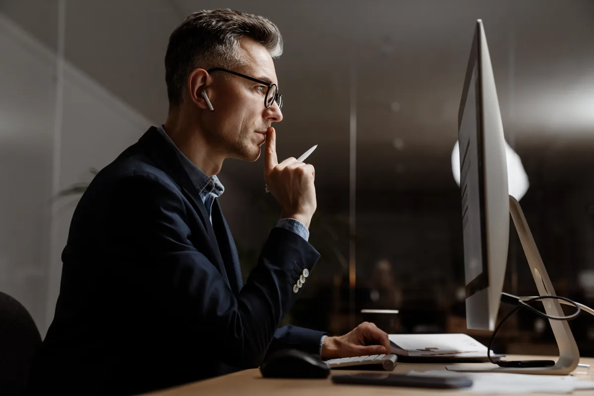 Gérant de TPE concentré seul devant son écran, lumière tamisée, AirPod, il gère tout